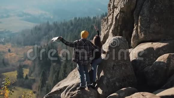 年轻的旅游夫妇相爱站在岩石上欣赏美丽的景色拜访著名游客的男人和女人视频的预览图
