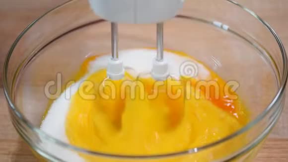 在木制背景桌上的一个玻璃碗里用糖打蛋黄的女人的手紧紧地抓住视频的预览图