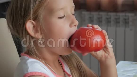 有趣的小女孩坐在厨房的桌子上吃有机蔬菜成熟的红色番茄视频的预览图