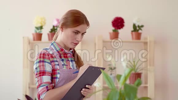 小生意开一家花店一个穿着格子衬衫和条纹围裙的女孩拿着一个纸签微笑着视频的预览图