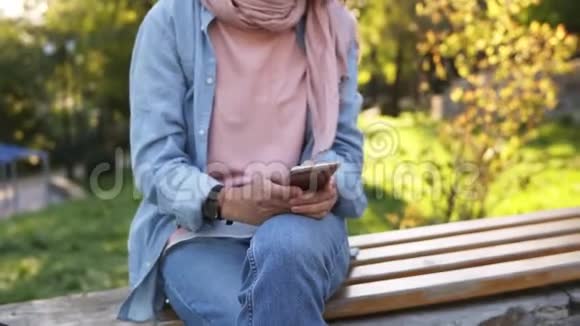 体贴的女孩坐在城市公园的长凳上旁边有她徒步旅行的自行车看着她的手机穿着视频的预览图