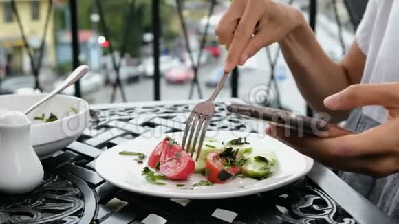女人用电话在街上的一家餐馆吃蔬菜沙拉视频的预览图