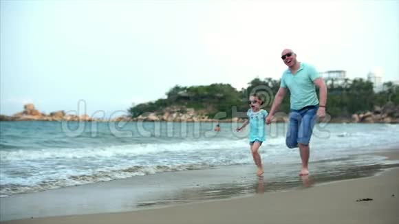 年轻的家庭父亲和女儿沿着海岸奔跑幸福的家庭沿着海岸散步视频的预览图