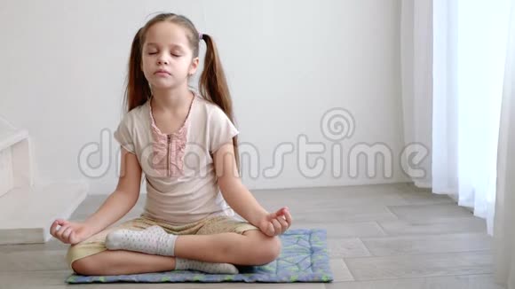 小可爱的女孩坐在瑜伽莲花的姿势在窗户附近冥想视频的预览图
