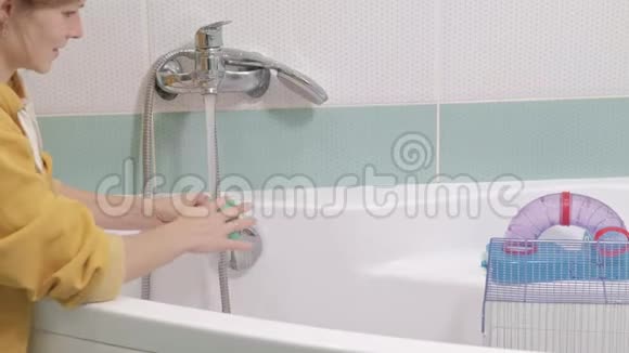 一个年轻的女人照顾一只宠物用水清洗水龙头下的食物碗打扫浴室里的笼子一个视频的预览图