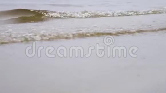 靠近沙滩上的河浪库存录像小浪淘沙在浅棕色的沙滩上冲刷着河岸视频的预览图