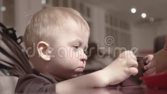 可爱的小男孩坐在咖啡馆里和父母通电话看动画片视频的预览图