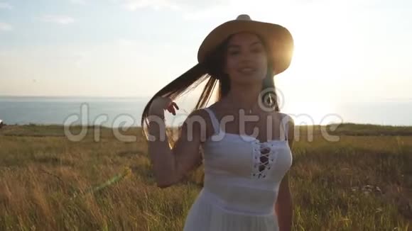 穿着白色浅色短裙和帽子的迷人的黑发女郎在田野里旋转视频的预览图