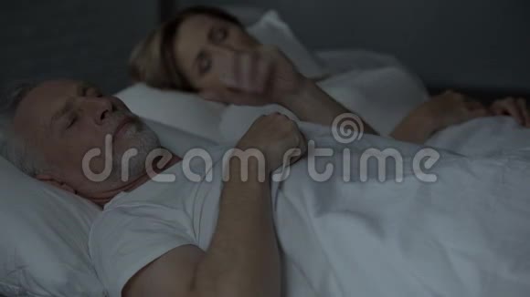 醒着老人揉着头看着睡在旁边的女人烦恼视频的预览图