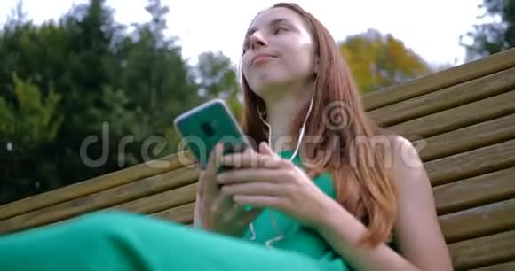年轻女子躺在长凳上用耳机听音乐视频的预览图