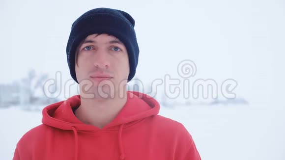 戴着黑色帽子的年轻人的肖像看着冬天寒冷的室外镜头视频的预览图