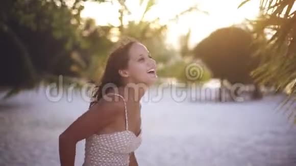 快乐的年轻美丽的女人穿着漂亮的裙子在阳光下在热带棕榈树之间跳舞享受着他在度假的时光视频的预览图