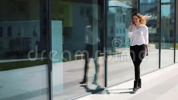 快乐的年轻女孩在智能手机上交谈走在办公室中心附近的街道上穿着商务服装的女人视频的预览图