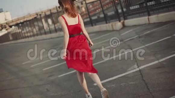 迷人的年轻红发女人穿着红色的裙子在街上奔跑在日落时玩得很开心慢动作视频的预览图