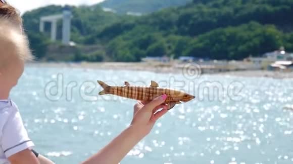 年轻的妈妈带着小儿子在大海的背景上玩玩具鱼视频的预览图