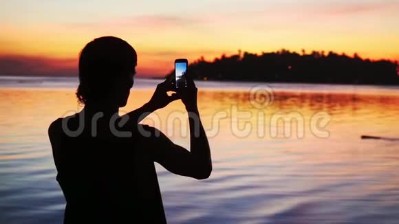 年轻人的剪影用手机在美丽的日落背景上拍照慢动作1920x1080视频的预览图