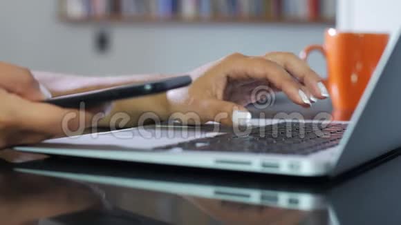 笔记本电脑和智能手机上女性手打字的特写视频的预览图
