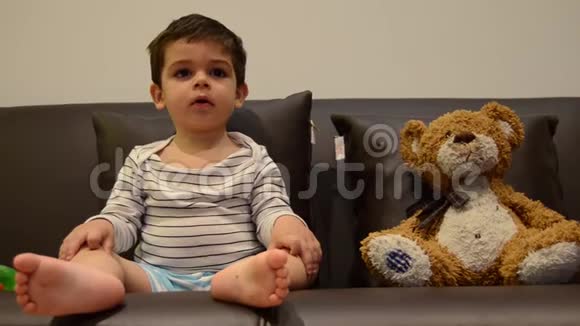 可爱的两岁男孩和他的泰迪熊一起看电视视频的预览图