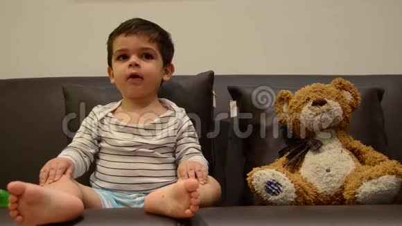 可爱的两岁男孩和他的泰迪熊一起看电视视频的预览图