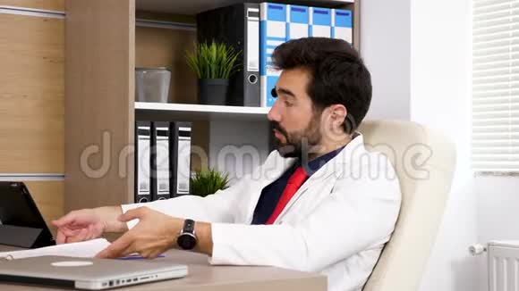 他办公室里的医生坐在椅子上和他的办公桌谈话视频的预览图