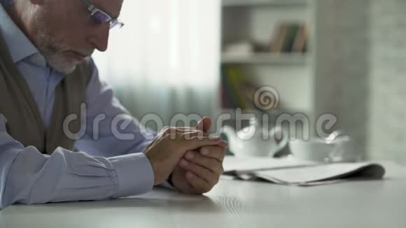 老年男性坐在桌子旁搓手摘下眼镜忧心忡忡视频的预览图