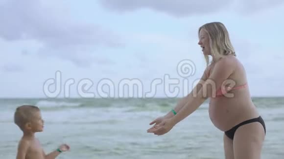 年轻的怀孕妈妈和她的儿子在海滩上玩和玩视频的预览图