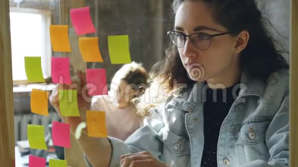 与女性合作时为年轻的创意企业家在玻璃板上贴上彩色贴纸做特写视频的预览图
