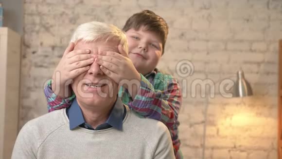 年轻的胖孩子用手闭上祖父眼睛猜猜是谁游戏恶作剧幸福的家庭观念家庭视频的预览图