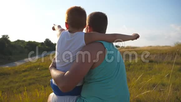 父亲和他的小儿子一起在户外度过时光爸爸和孩子坐在山上的绿草旁指着视频的预览图