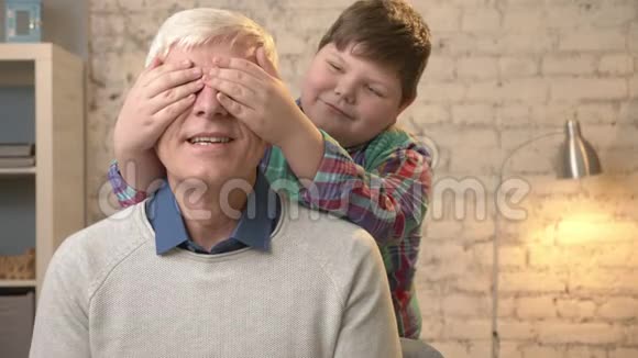 年轻的胖孩子用手闭上祖父眼睛猜猜是谁一场游戏恶作剧孙子看着摄像机视频的预览图