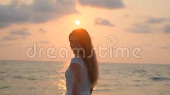 穿着白裙子的年轻漂亮女孩在海滩上散步海洋视频的预览图