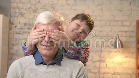 年轻的胖孩子用手闭上祖父眼睛猜猜是谁一场游戏恶作剧孙子看着摄像机视频的预览图
