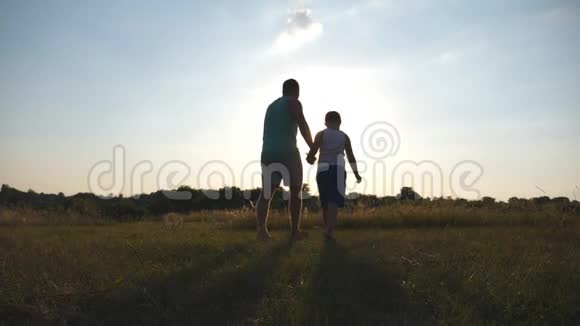 日落时分父亲和儿子在田野上散步互相牵着手的剪影快乐的家庭花时间视频的预览图