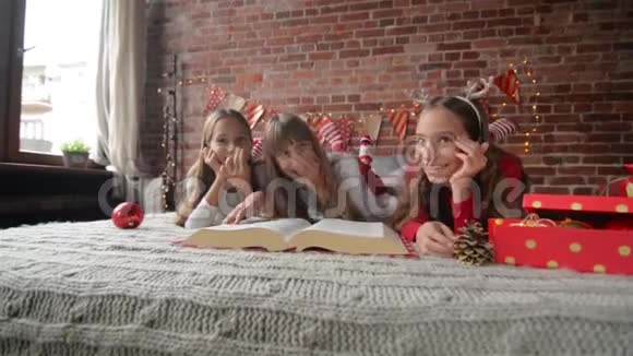 三姐妹躺在柔软的睡衣的床上三胞胎读一本巨大的圣诞故事书卧室装饰着视频的预览图