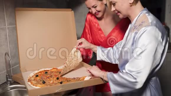 两个女朋友在外出前吃披萨和享受晚会聊天一个穿着蓝色晨衣视频的预览图