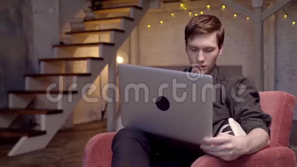 年轻人坐在沙发上用笔记本电脑工作库存录像年轻的自由职业者正全神贯注地工作在笔记本电脑上视频的预览图