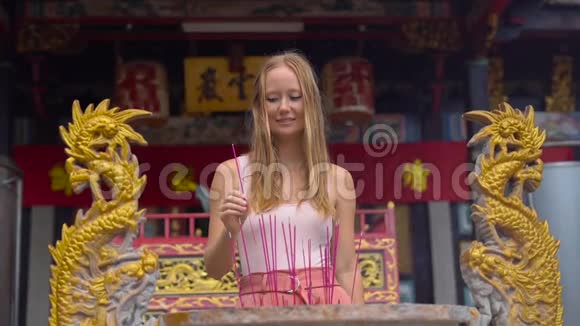 一位年轻女子在一座佛寺中慢镜头放着一根香棒香炉视频的预览图