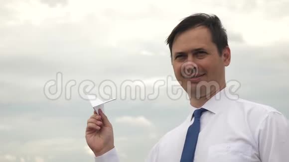 穿着白色衬衫和领带的商人正在玩纸飞机在乌云的背景下微笑视频的预览图