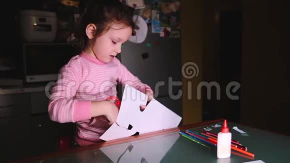 漂亮的欧洲学龄前小女孩穿着粉色毛衣坐在家里的桌子旁剪着纸的形状视频的预览图