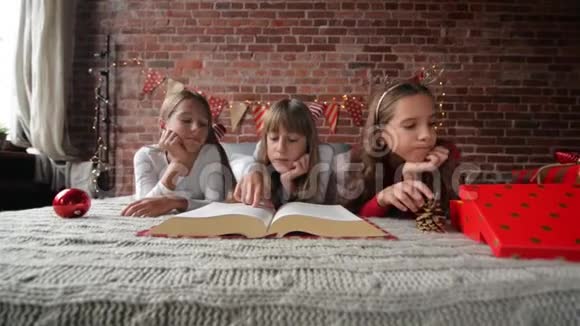 三姐妹躺在柔软的睡衣的床上三胞胎读一本巨大的圣诞故事书卧室装饰着视频的预览图