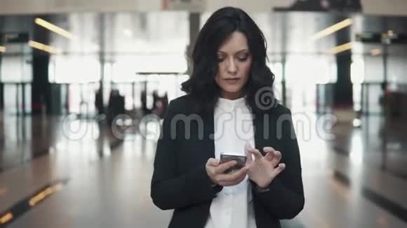 一个穿着西装的女人穿过一座现代化办公楼的大厅女商人用手机视频的预览图