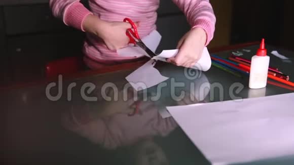 一张可爱的学龄前女孩的特写照片她穿着粉色毛衣用剪刀从纸上剪下形状反射在玻璃桌上视频的预览图