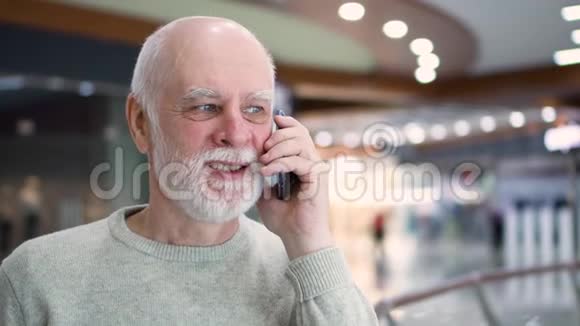 站在商场里微笑的老人用他的智能手机和朋友或家人聊天视频的预览图