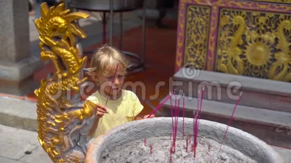 一个小男孩在佛寺里慢镜头在香炉里放一根芳香棒视频的预览图