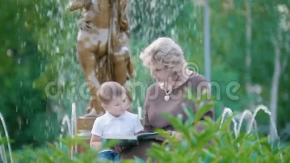 迷人的祖母和小男孩在夏天公园喷泉附近看书视频的预览图