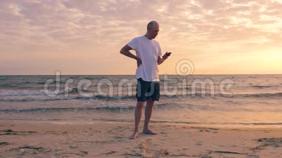 在海边美丽的日出时男人用手机视频的预览图