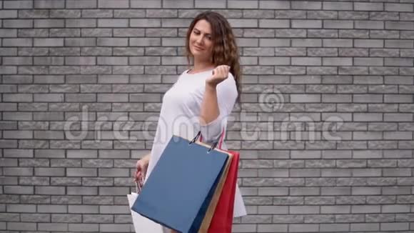 一个购物后带着包裹的女孩心情很好靠在石头墙上慢动作视频的预览图