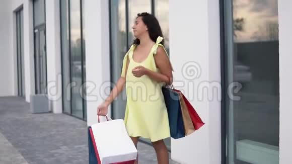 漂亮的女孩模特穿着一件长裙购物后手里拿着彩色袋子心情很好慢动作高清高清视频的预览图