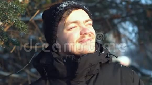 微笑着穿着黑色夹克的年轻人在冬天的森林里向远处望去特写镜头视频的预览图