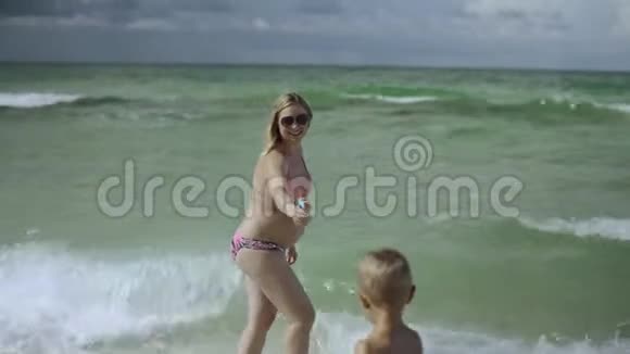 年轻的怀孕妈妈和她的儿子在海滩上玩和玩视频的预览图
